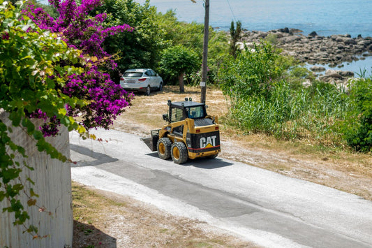 PLACEHOLDER - skid steer loader on a road with heavy roadside foliage